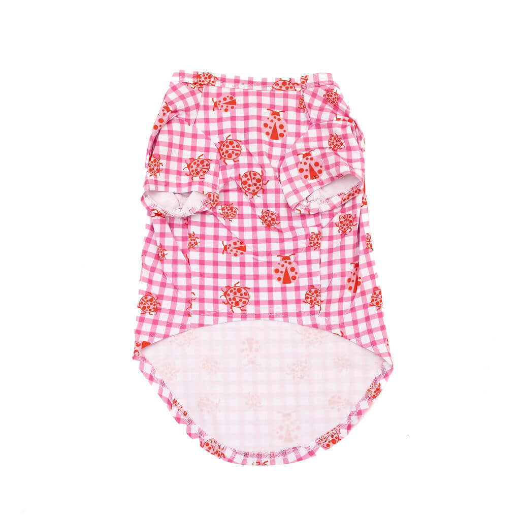 Flat lay of the front of a pink gingham ladybug dog shirt showing shortened hem design, on a white background.