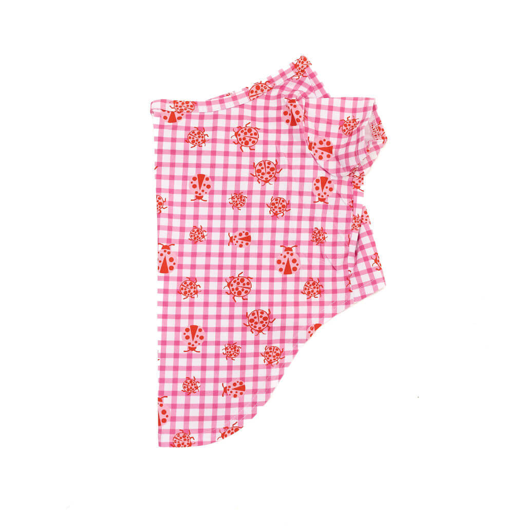 Side view flat lay of a pink gingham dog shirt with red ladybug print, on a white background.
