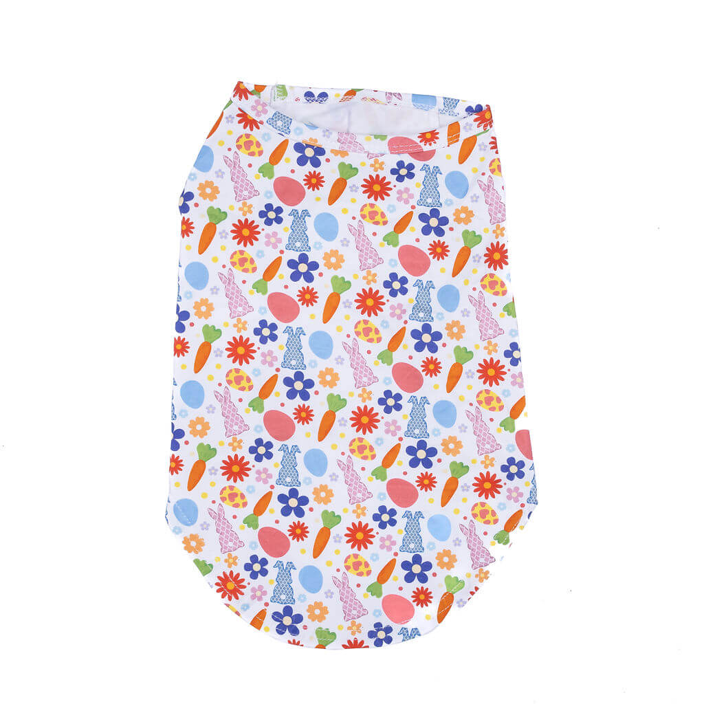 Sleeveless, white dog t-shirt with a vibrant, all-over print featuring pink rabbits in various poses, blue and purple flowers with yellow centers, orange carrots with green tops, and light blue and pink Easter eggs. The shirt is laid flat and shown from a front-facing perspective.