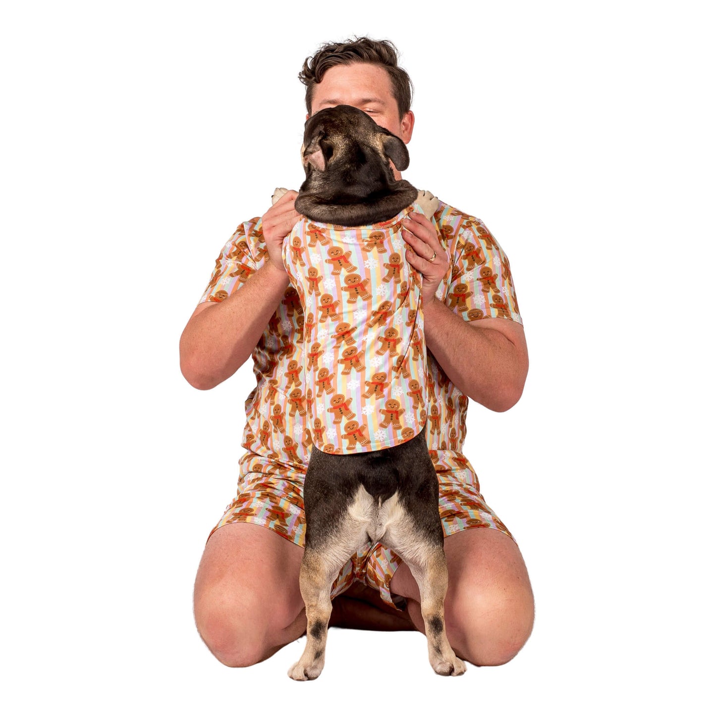 A French Bulldog stganding on Hind legs cuddling his dad. They are wearing GIngerbread Cheer matching pyjamas.