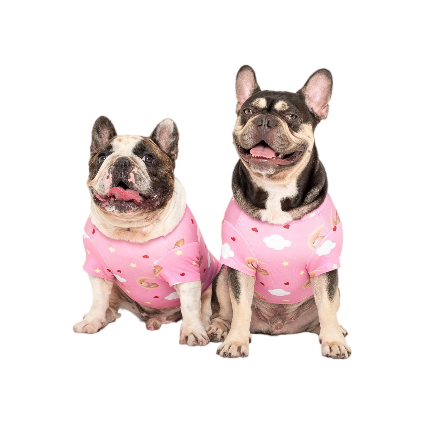 Two French Bulldogs sitting down wearing Vibrant Hound's Lil Dreamer dog pyjamas. They are pink with white clouds, love hearts, and stars.